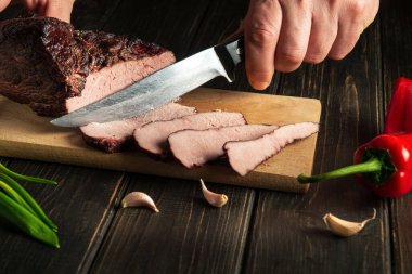 Aşçı, şenlikli bir akşam yemeği için ahşap bir kesme tahtasıyla pişmiş eti keser.