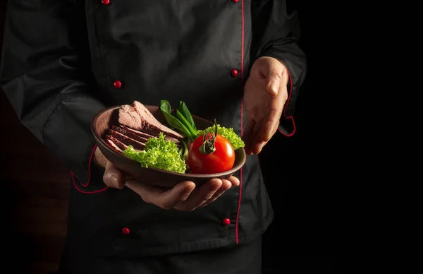 Plate with food in the chef hand. Dark background free space for advertising