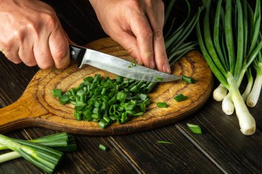 Şefin elleriyle vejetaryen yemeği pişirmek için kesme tahtasındaki taze soğanları bıçakla dilimlemek. Köylü yemeği..