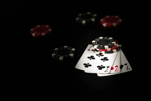 Playing cards on a black table with a winning combination three of a kind or set in game poker and chips in the background