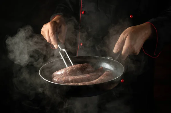 The chef flips the meat sausage in a hot pan with a fork. Preparing a delicious meal in the kitchen.