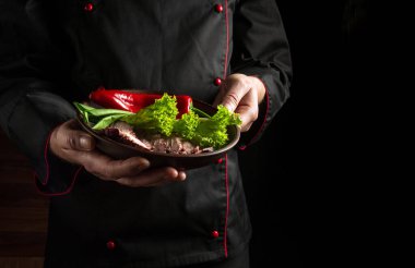 The chef presents his dish on a plate of sliced baked steak and vegetables. Space for hotel menu or recipe on dark background