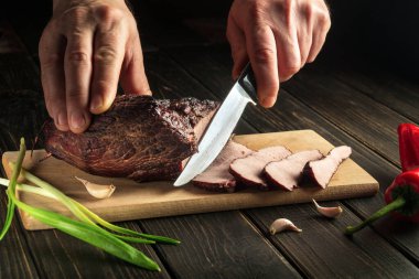 Lezzetli bir öğle yemeği için mutfak tahtasındaki füme eti dilimlemek. Bıçaklı bir şefin yakın çekimi..