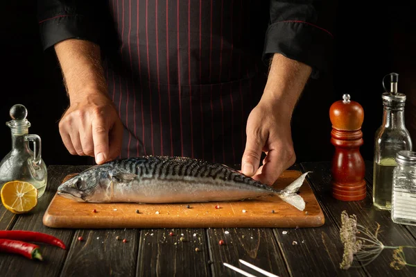 Fish Chef prepares mackerel or Scomber in the hotel kitchen. The concept of cooking fish on a dark background. European cuisine.