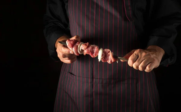 The chef is holding a shish kebab with raw lamb meat and onions on a skewer. Caucasian national cuisine