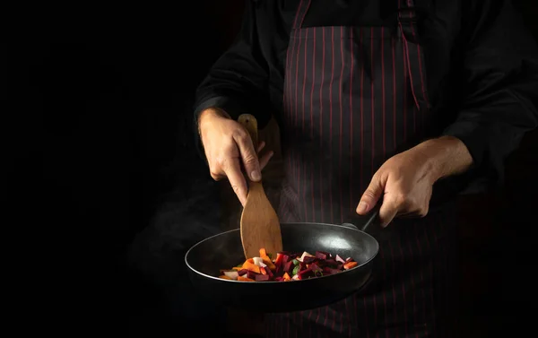 Cooking vegetables in a frying pan in the hands of a chef for a vegetarian food. Advertising space on a black background