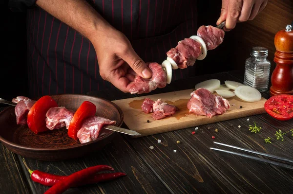 The process of cooking meat kebab in the restaurant kitchen. The chef spears raw lamb meat on a skewer with onions.