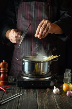 Mutfakta, diyet çorbası aşçının elleriyle sıcak bir tencerede hazırlanır. Şef yemeğe tuz ekliyor..