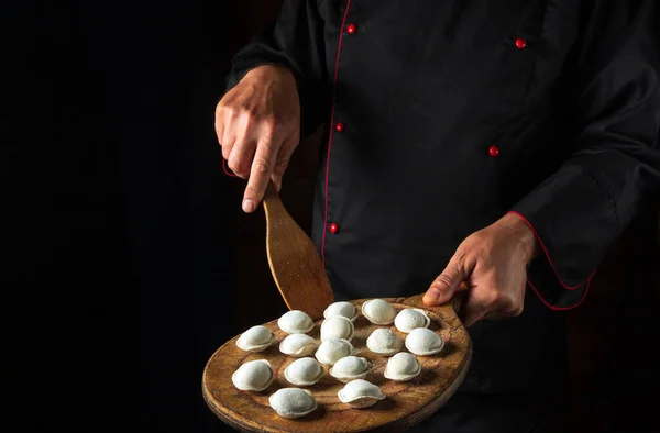 Cooking dumplings by the hands of the chef in the kitchen of the hotel. Free space for advertising. Delicious lunch concept on black background.