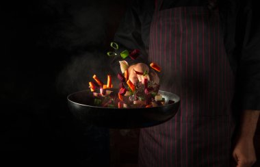 Aşçı sebzeleri kızartma tavasında hazırlar. Sağlıklı vejetaryen yemekleri ve yemekleri karanlık bir arka planda pişirmek. Ücretsiz reklam alanı.