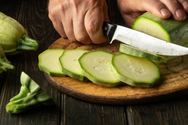 Bıçaklı bir şefin elleri vejetaryen yemeği hazırlamadan önce tahta kesme tahtasıyla sebze iliği kesiyor..