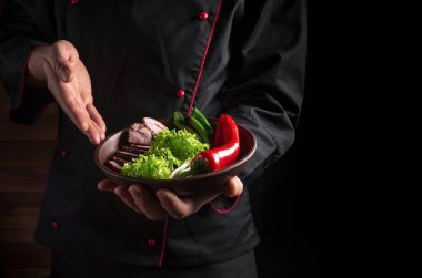 Sunum için şefin elinde yemek tabağı. Reklamcılık için karanlık arkaplan boşluğu.
