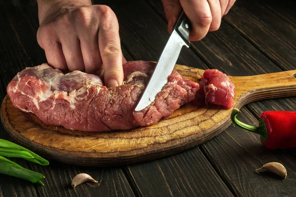 Butcher or chef cuts raw beef meat on a cutting board before baking. Hotel menu recipe idea