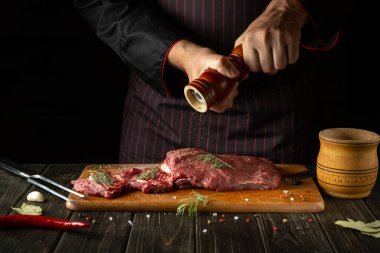 The chef adds pepper to raw beef meat on a cutting board before barbecue. Recipe idea for a restaurant or hotel.