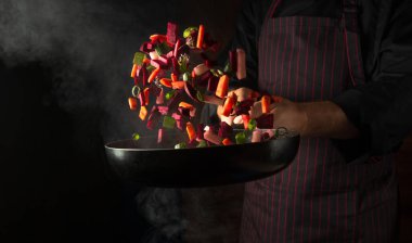 Cooking vegetables in a frying pan in the hands of a chef for a vegetarian food. Advertising space on a black background