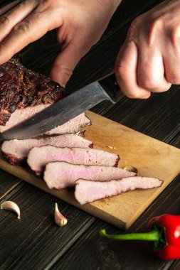 The chef cuts the baked beef meat into small pieces on the cutting board of the kitchen. Top view cooking process concept