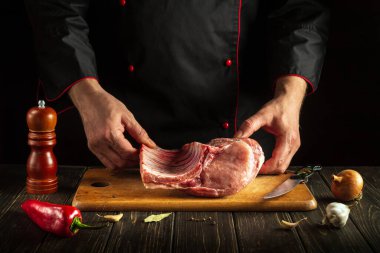 Experienced chef is holding a piece of raw meat with a bone in the kitchen. Pork ribs in the butcher's hands