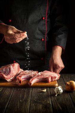 Chef sprinkles raw ribs with salt. The concept of cooking delicious food for the hotel or restaurant