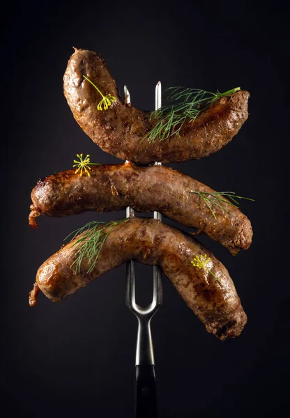 Delicious homemade meat sausages on a fork. The idea of a delicious lunch for a hotel on a black background.