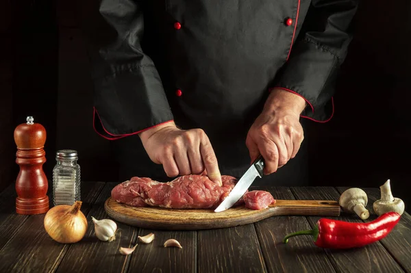 Butcher or or chef cuts raw beef meat on a cutting board before baking. Hotel menu recipe idea
