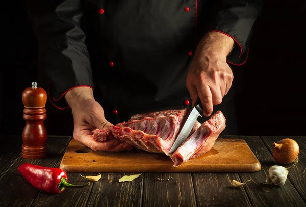 Butcher cuts raw ribs on a cutting board before barbecuing. Cooking delicious food in the hotel kitchen