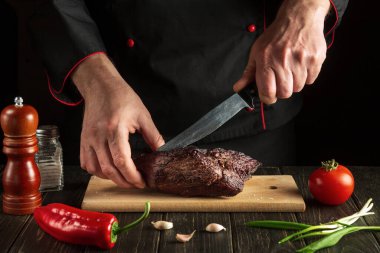 Professional chef slicing beef steak with knife on wood cutting board. Food preparation process concept