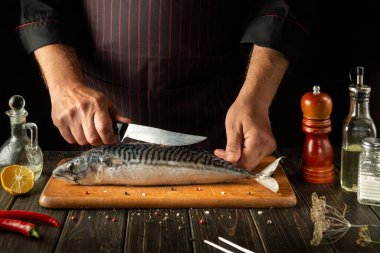 Fish Chef cooks Scomber or mackerel in the kitchen. The concept of cooking fish food for a restaurant or hotel. Knife in the cook hand.