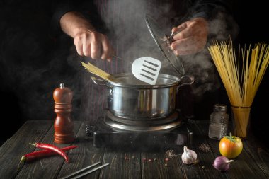 The chef cooks a delicious soup with vegetables and pasta in a hot pot in the kitchen. Delicious hotel food recipe.