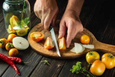 Preservation of tomatoes in a jar. Chef hands cuts a tomato on a kitchen cutting board. Peasant food