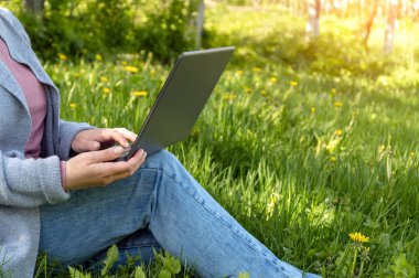 Work with a laptop outdoors in a park on a sunny day. Cropped section of female freelancer working outdoors