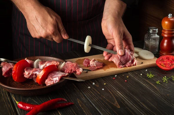 The chef prepares shish kebab with raw lamb meat and onions. Punching meat on a skewer by the hands of a cook. Caucasian national cuisine