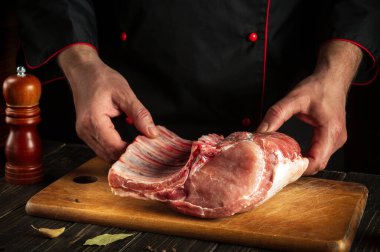 Şef bir parça çiğ eti kemikle tutuyor. Kasap ellerinde domuz pirzolası. Asya mutfağı.