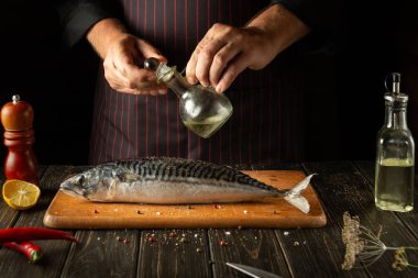 Chef adding oil to mackerel fish on hotel kitchen cutting board. Scomber is the best for cooking delicious lunch.