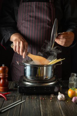 The chef cooks soup with pasta and vegetables in a saucepan. Recipe for a delicious lunch for a restaurant or hotel