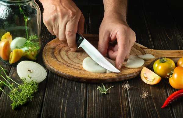 Cooking pickled vegetables in a jar. The cook cuts the onion with a knife on the cutting board of the kitchen. Close-up of chef hands while working