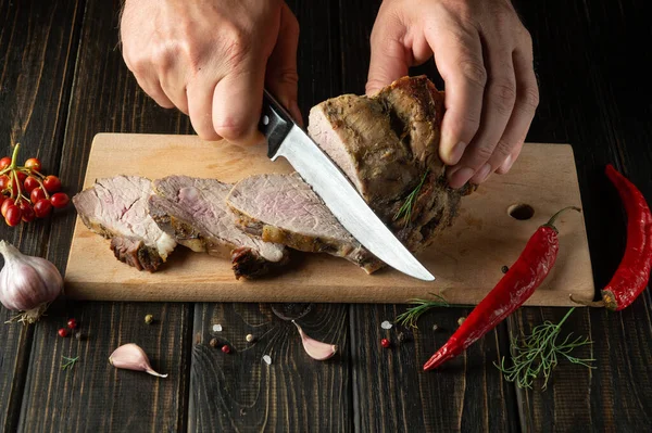 Slicing juicy beef steak with a knife in the hands of a chef close-up. The concept of cooking. Dark background for advertising or recipe.