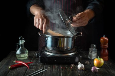 The chef cooks a delicious soup with vegetables in a hot pot. Work environment on the kitchen table. Menu for the hotel.