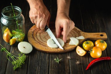 Cooking ajika with onions, tomatoes and hot peppers. The chef cuts the onion with a knife on the kitchen cutting board. Asian food.