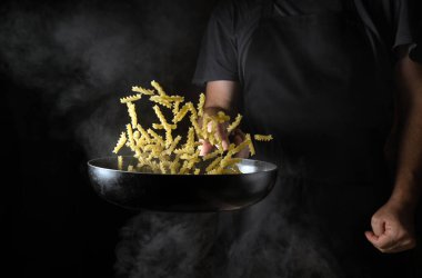 Cooking noodles in the kitchen of a restaurant or hotel. The chef tosses food on a hot pan. Place for advertising on a black background.