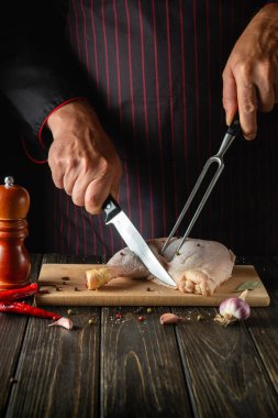 The chef cuts a chicken leg in the kitchen. The concept of a recipe for a delicious chicken meal with spices for a hotel or restaurant