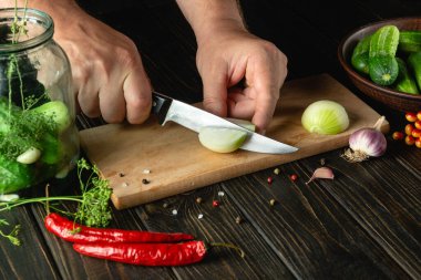 Slicing onions on a cutting board by the hands of a cook for pickling or salt in a jar with cucumbers and spices. Menu for restaurant or hotel.