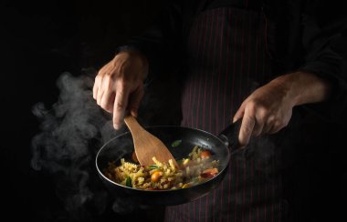 Cooking fresh vegetables and pasta with spices. The chef flips food on a hot pan. Thai street food.