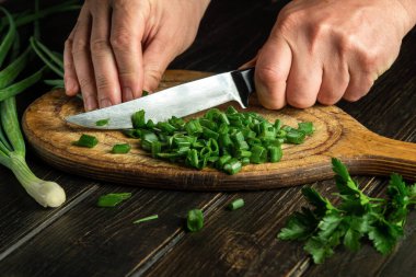 The cook cuts green onions on a wooden cutting board with a knife for cooking vegetarian food. Peasant dish