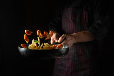 The chef throws food on a hot pan. Thai street food pasta with spices and vegetables. Space for advertising on a dark background.