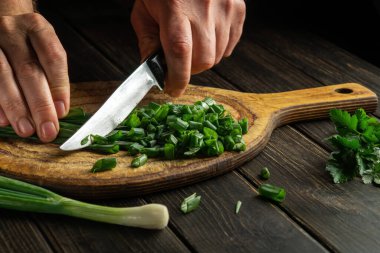 The cook cutting green onion on a cutting board with a knife for preparing a vegetarian dish. Peasant food