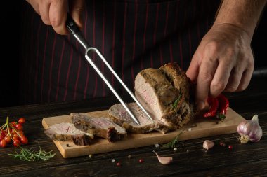 Grilled juicy beef steak. Sliced meat on a cutting board. Fork in chef hand on dark background.