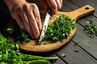 Slicing green parsley on a cutting board with a knife for cooking vegetarian food cook hands.