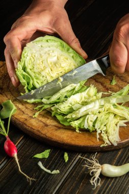 Slicing with a knife fresh cabbage by chef hands before preparing national or vegetarian food. 