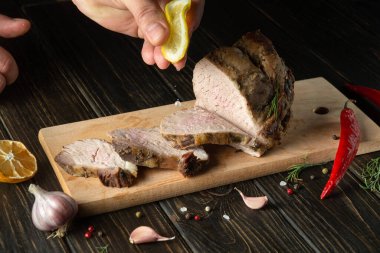 Chef squeezes fresh lemon juice onto the grilled sliced beef. Place for advertisement or prescription on dark background.