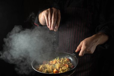 Cooking fresh vegetables and pasta. The chef adds salt to a steaming hot pan. Thai Restaurant Cuisine.